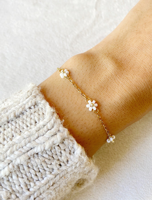 Gold bracelet with white flowers and beads on a wrist against a light background